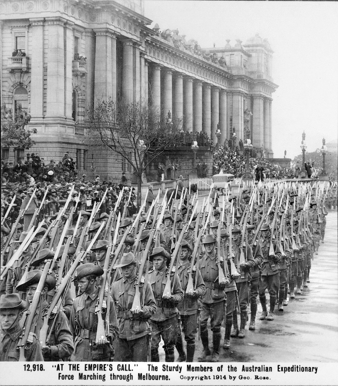 大约在 1914 年 8 月，AIF 士兵在启程前往海外服役之前，肩上扛着上了刺刀的步枪，行进经过维多利亚州墨尔本的议会大厦。 作者 澳大利亚摄影师
