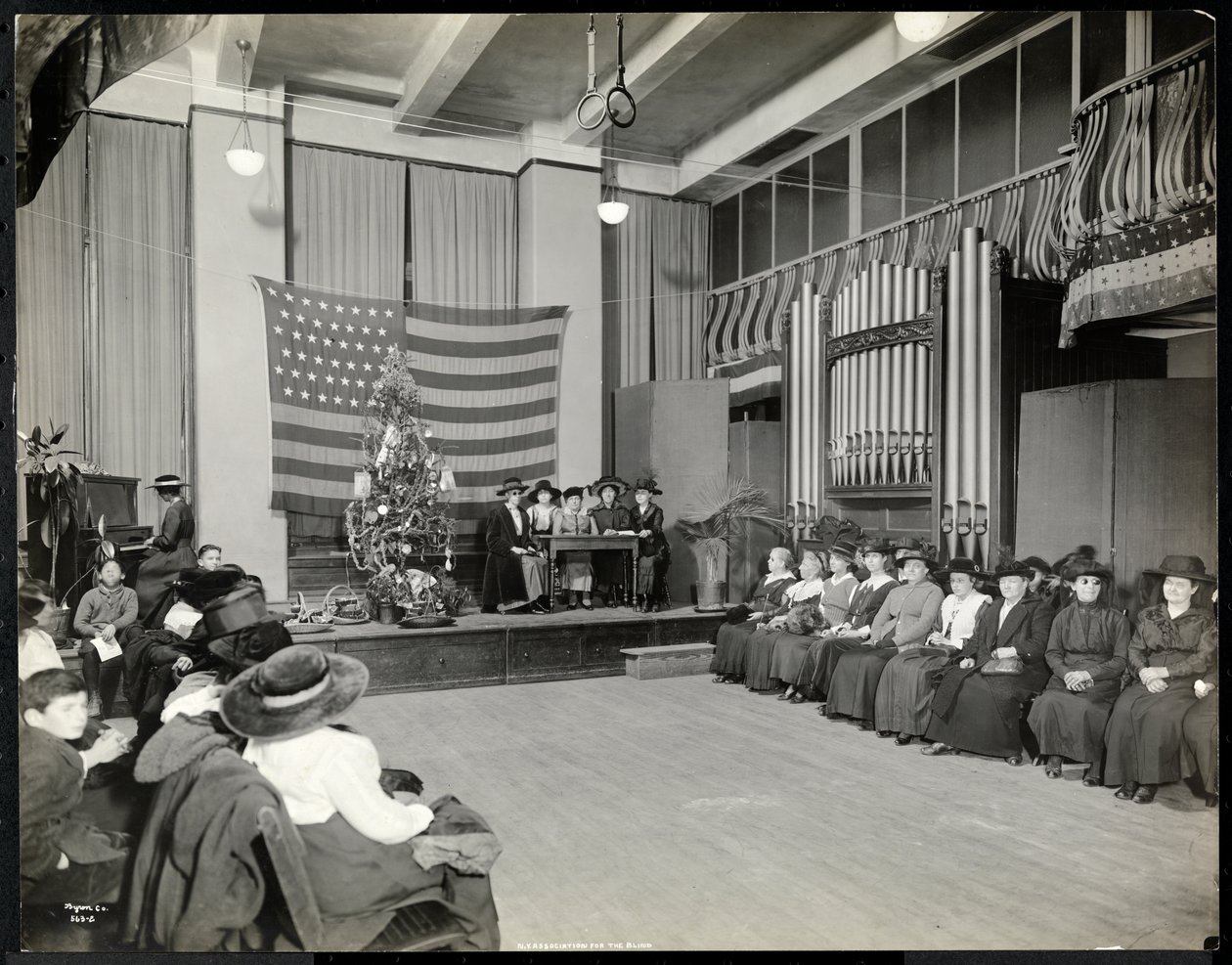人们在纽约盲人协会的礼堂与圣诞树和人们可能在舞台上演奏器官，1920年（银色明胶印刷） 作者 拜伦公司