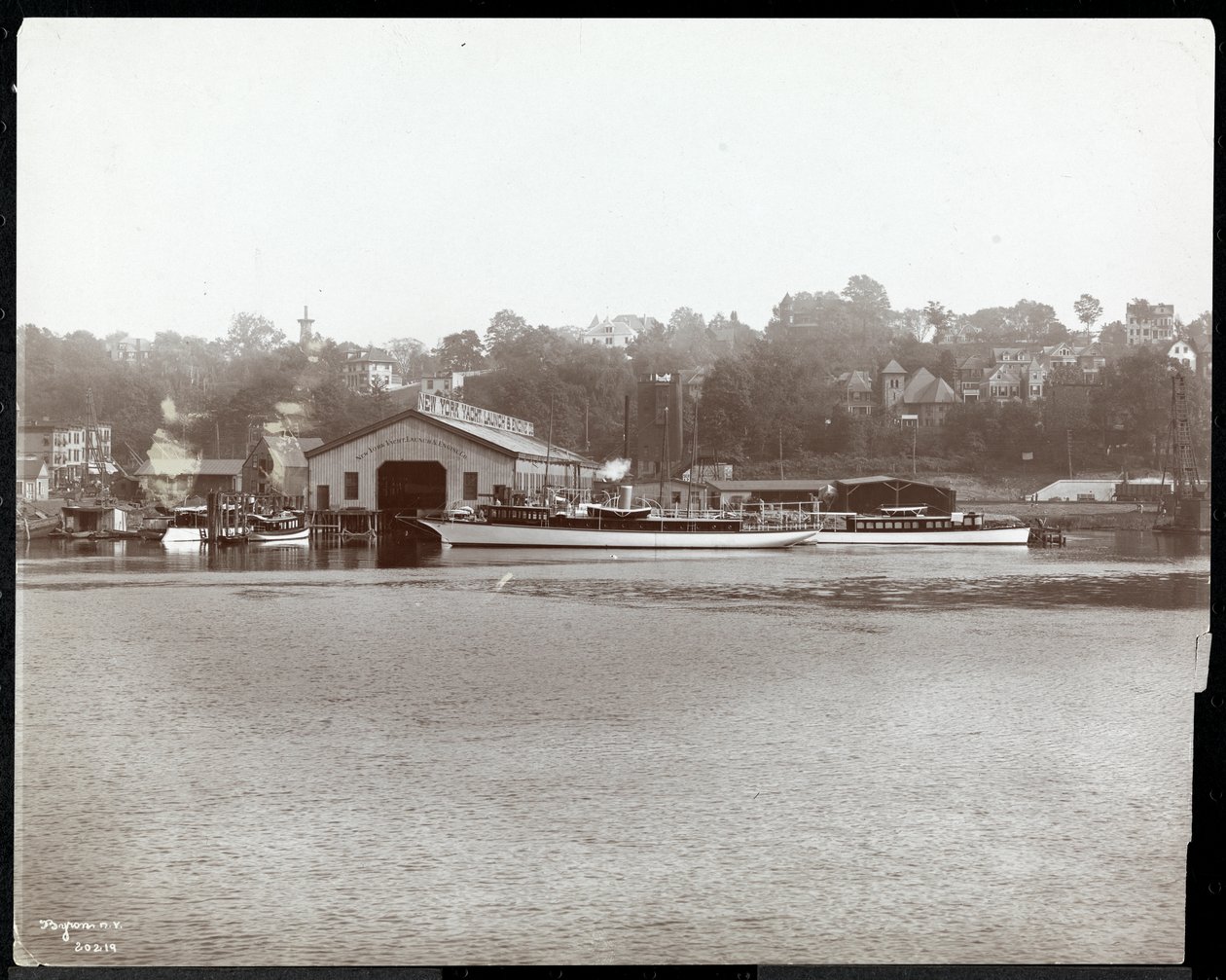 1905年纽约哈莱姆河上的纽约游艇，发射和发动机公司的码头和船只的视图（银色明胶印刷） 作者 拜伦公司