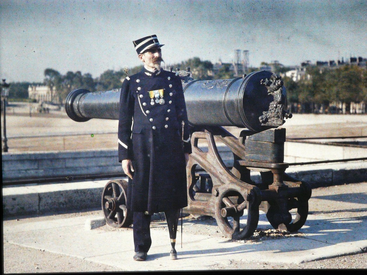 1918年，一名穿着制服并带着三枚奖牌的士兵站在巴黎的一门大炮旁边（自动着色） 作者 朱尔斯·格维斯·考特莱蒙