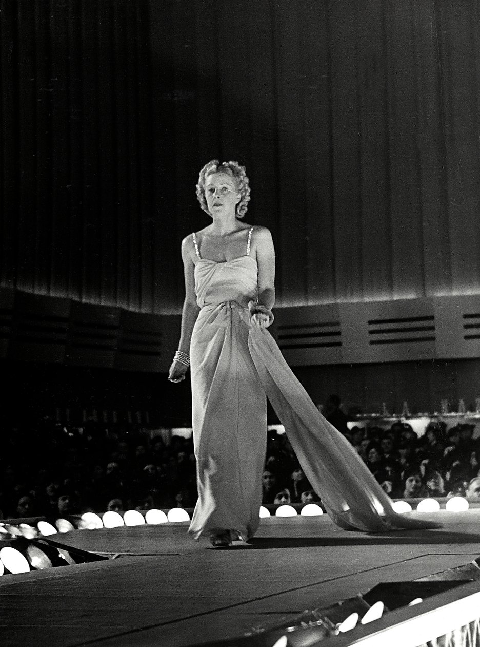 Model photographed on a runway in evening dress with rhinestone shoulder straps; the article is a creation of the couture house "Fumach". (b/w photo) 作者 路易斯·波吉诺（Luis Bogino）