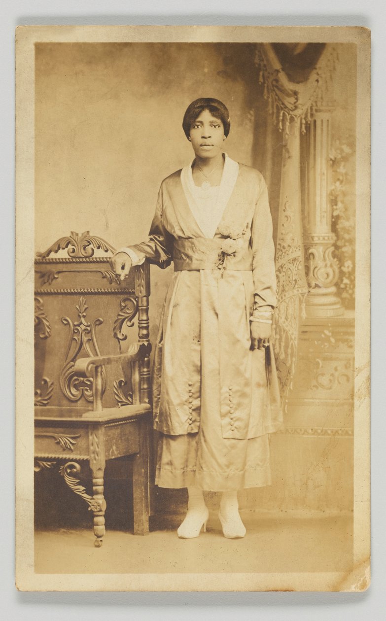 1904-1918年的摄影明信片，一个女人站在一张木椅旁边。 作者 不明