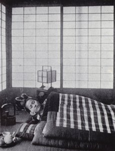 Girl asleep between wadded quilts with a wooden pillow (b/w photo)