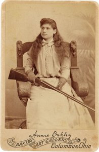 安妮-奥克利 : Annie Oakley:.这位传奇的神枪手端庄地坐在一张文艺复兴风格的大椅子上，膝上放着一把猎枪。她精致的女性特征和飘逸的秀发掩盖了她粗犷的户外形象 ©Buyenlarge/UIG/Leemage 作者 American Photographer