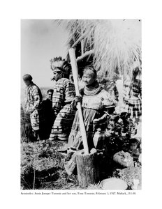 Annie Jumper Tommie使用砂浆和pestel制作玉米面，她的儿子Tony Tommie戴着鹰羽毛帽，1927年2月5日
