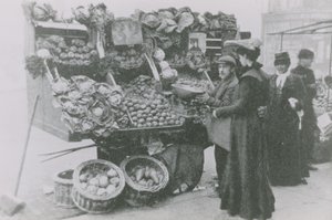 当他为女人服务时，杂货商站在他的摊位旁边 作者 英国摄影师