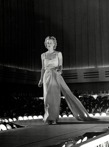 Model photographed on a runway in evening dress with rhinestone shoulder straps; the article is a creation of the couture house "Fumach". (b/w photo) 作者 路易斯·波吉诺（Luis Bogino）