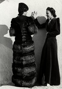 Two models present creations of the Italian couture house "Dragoni". One model seen from the back wears a silver fox coat. The other model wears a long velvet overcoat. (b/w photo) 作者 路易斯·波吉诺（Luis Bogino）
