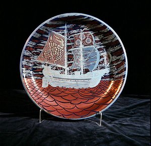 银色光泽的充电器，有一个大帆船在红色光泽的海面上航行（陶瓷）。 作者 威廉·德·摩根