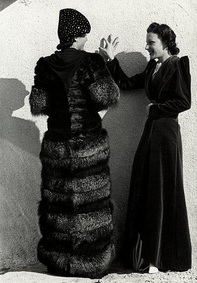 Two models present creations of the Italian couture house "Dragoni". One model seen from the back wears a silver fox coat. The other model wears a long velvet overcoat. (b/w photo) 作者 路易斯·波吉诺（Luis Bogino）