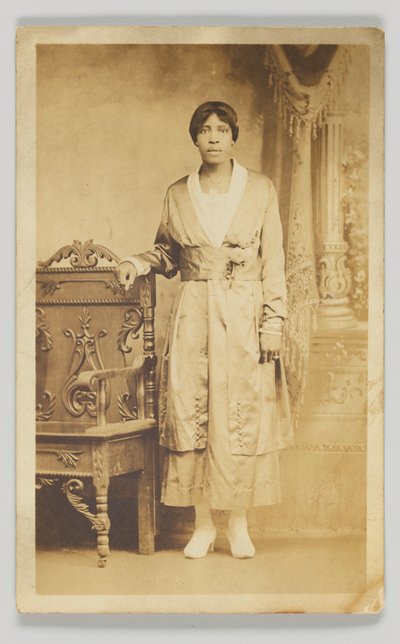 1904-1918年的摄影明信片，一个女人站在一张木椅旁边。 作者 不明