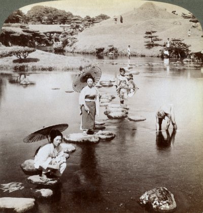1904年，日本熊本县水前寺花园，妇女们踩在垫脚石上穿过湖。 作者 安德伍德和安德伍德