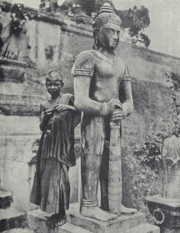 Young Buddhist novice monk beside a statue of the Buddha, French Indochina (b/w photo) 作者 尤因加洛韦